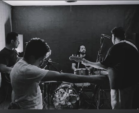 Cosmic Cactus and the Sandwaves rehearsing — black and white photo of the band around the drum kit, the bassist pointing his bass toward the drummer